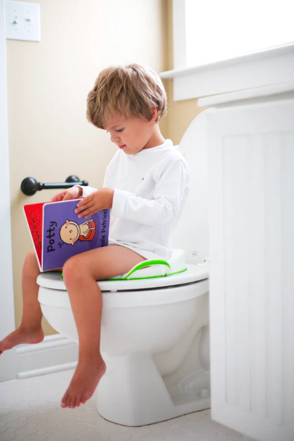 A young child sitting on the toilet, absorbed in a picture book about using the potty.